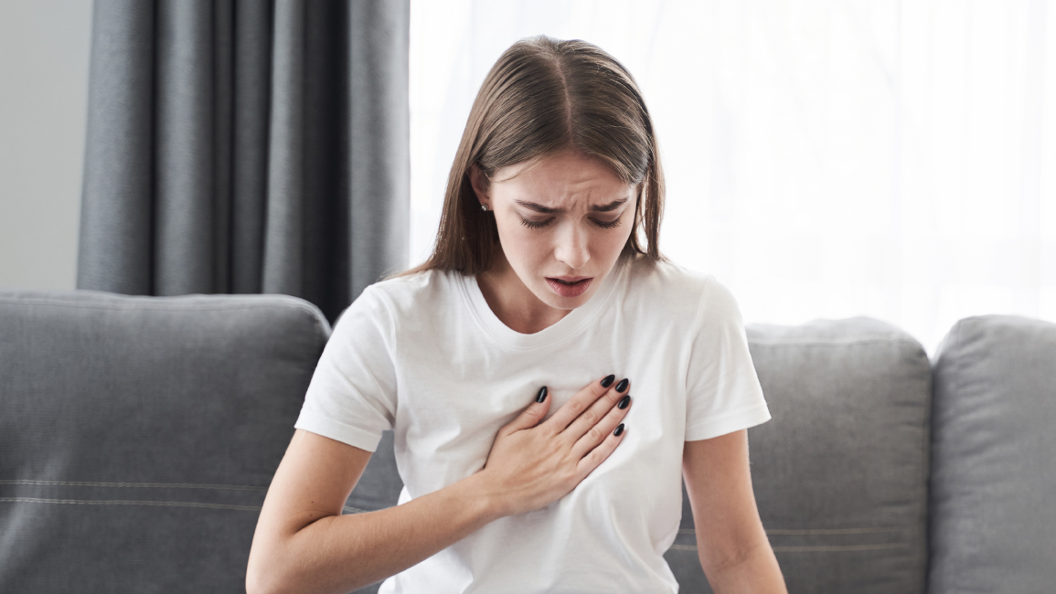 Adult experiencing subtle silent heart attack symptoms at home and reaching for her chest